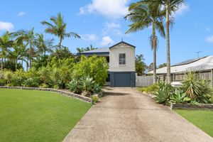 Charming Queensland home with lush green lawn, tall palm trees, and concrete driveway entrance.