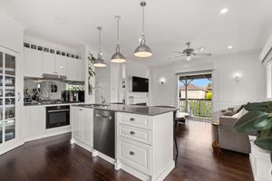 Classic white kitchen with dark stone island bench, stainless pendant lights, and hardwood timber floors.