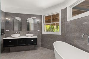 Modern bathroom with grey marble tiles, freestanding soaking tub, double vessel sinks, and arched mirrors.