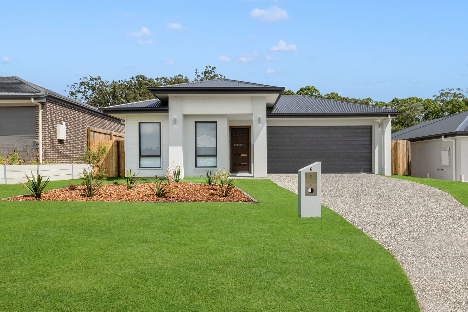Modern single-story home with dark roof, double garage, manicured lawn, and landscaped garden beds in a suburban setting.