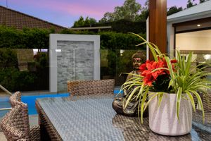 Outdoor patio with wicker furniture, Buddha statue, tropical plants, and water feature at sunset.