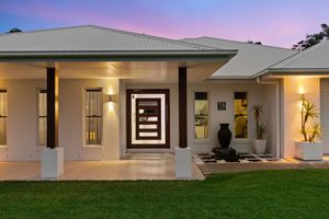 Modern home entrance with stylish front door, wall lighting, and manicured garden at dusk.
