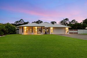 Spacious single-story home with lush green lawn and warm interior lighting at twilight.