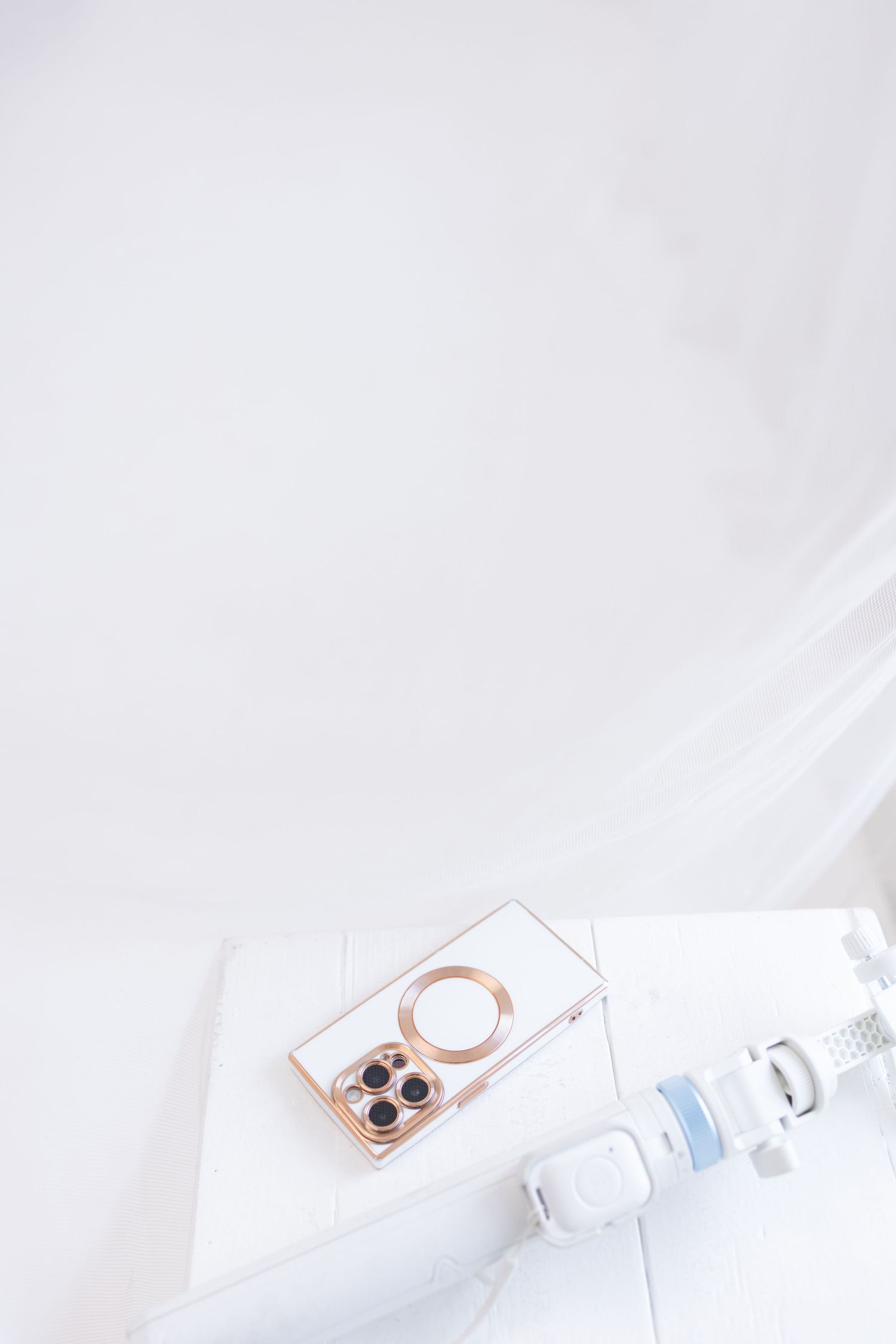 White table with Apple MacBook, DSLR camera, selfie stick, magazines, and a phone case with floral design.