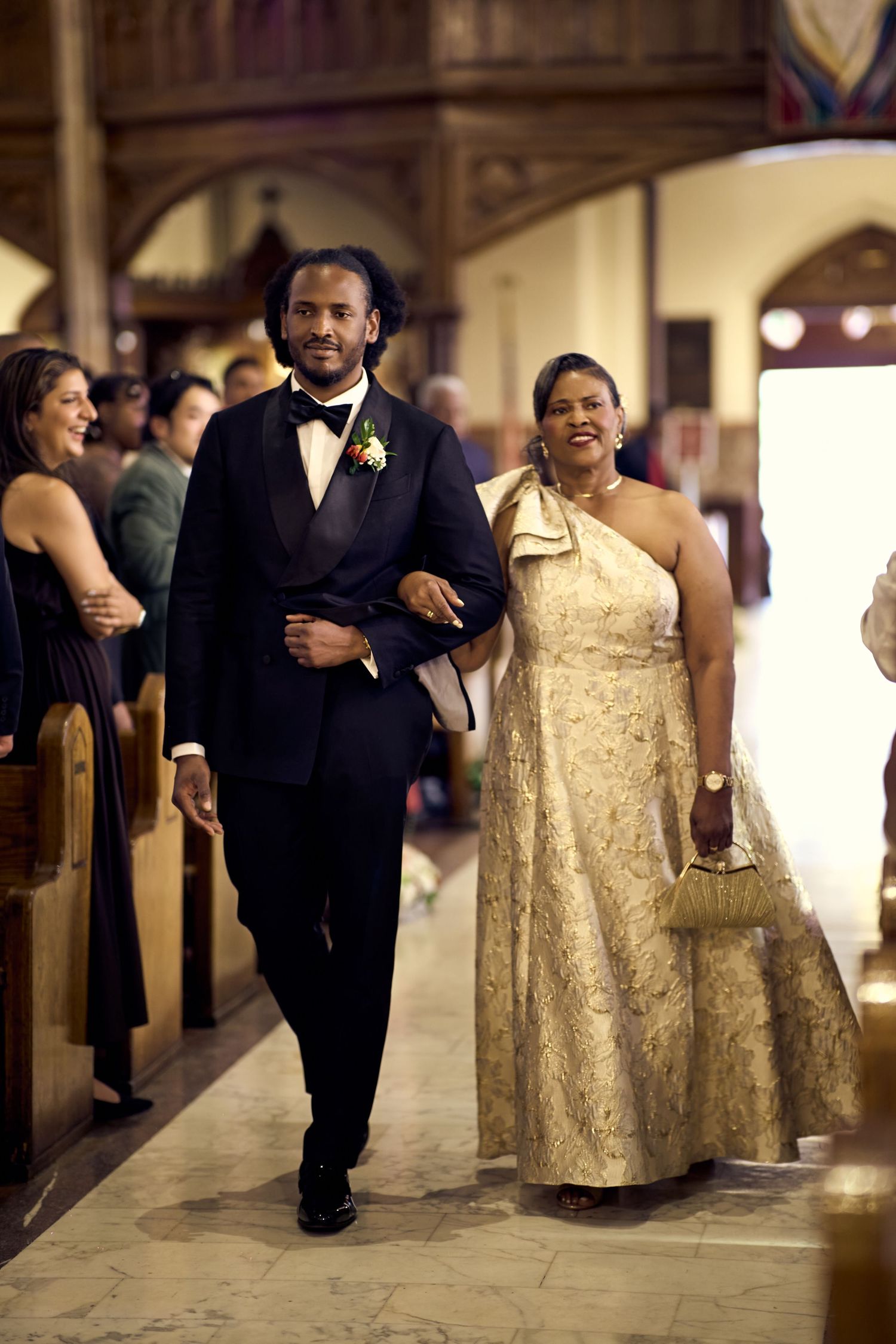 Groom in tuxedo escorts woman in floral gown down church aisle during elegant wedding ceremony.