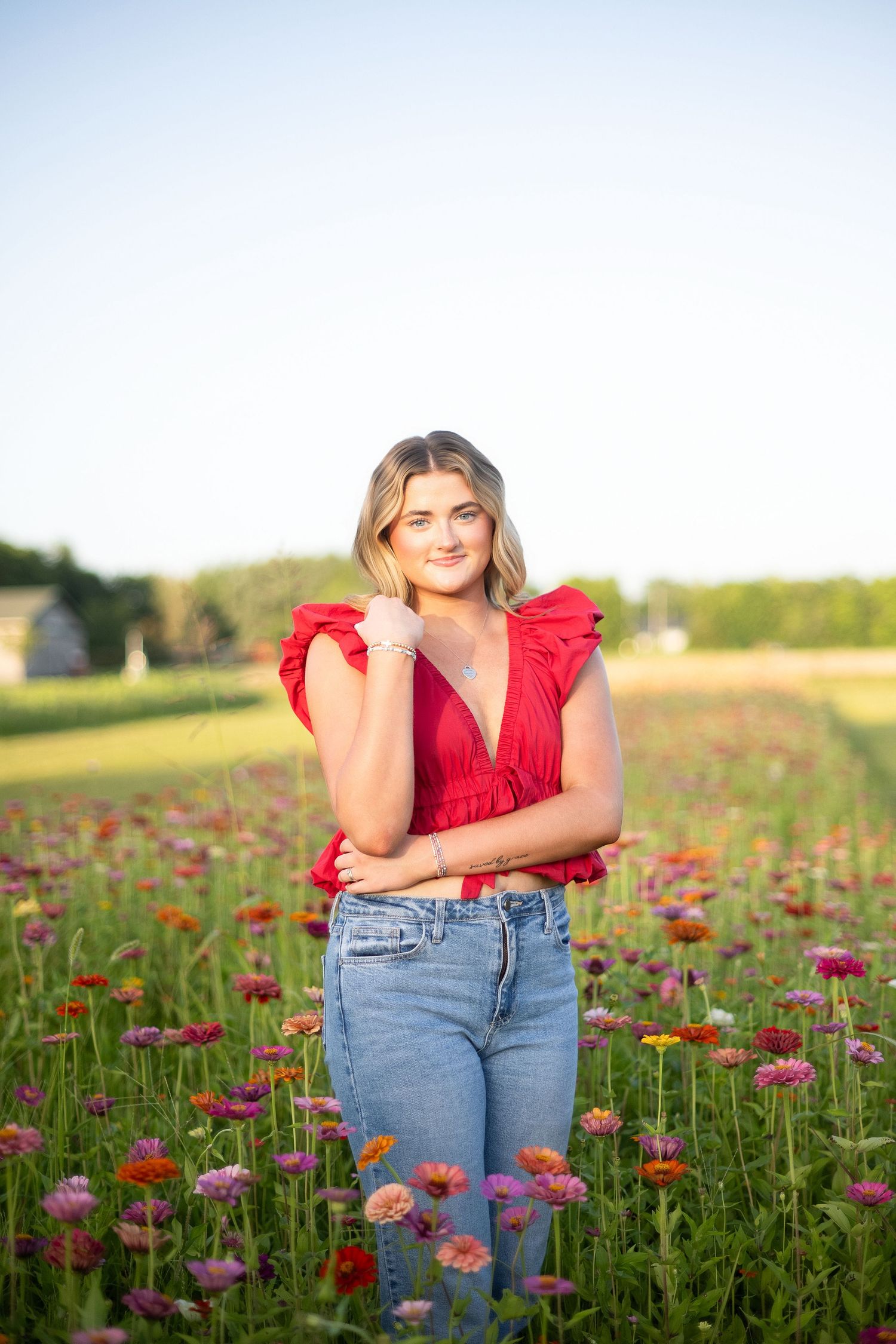 Young woman in red ruffled top and jeans posing in a colorful flower field during golden hour.