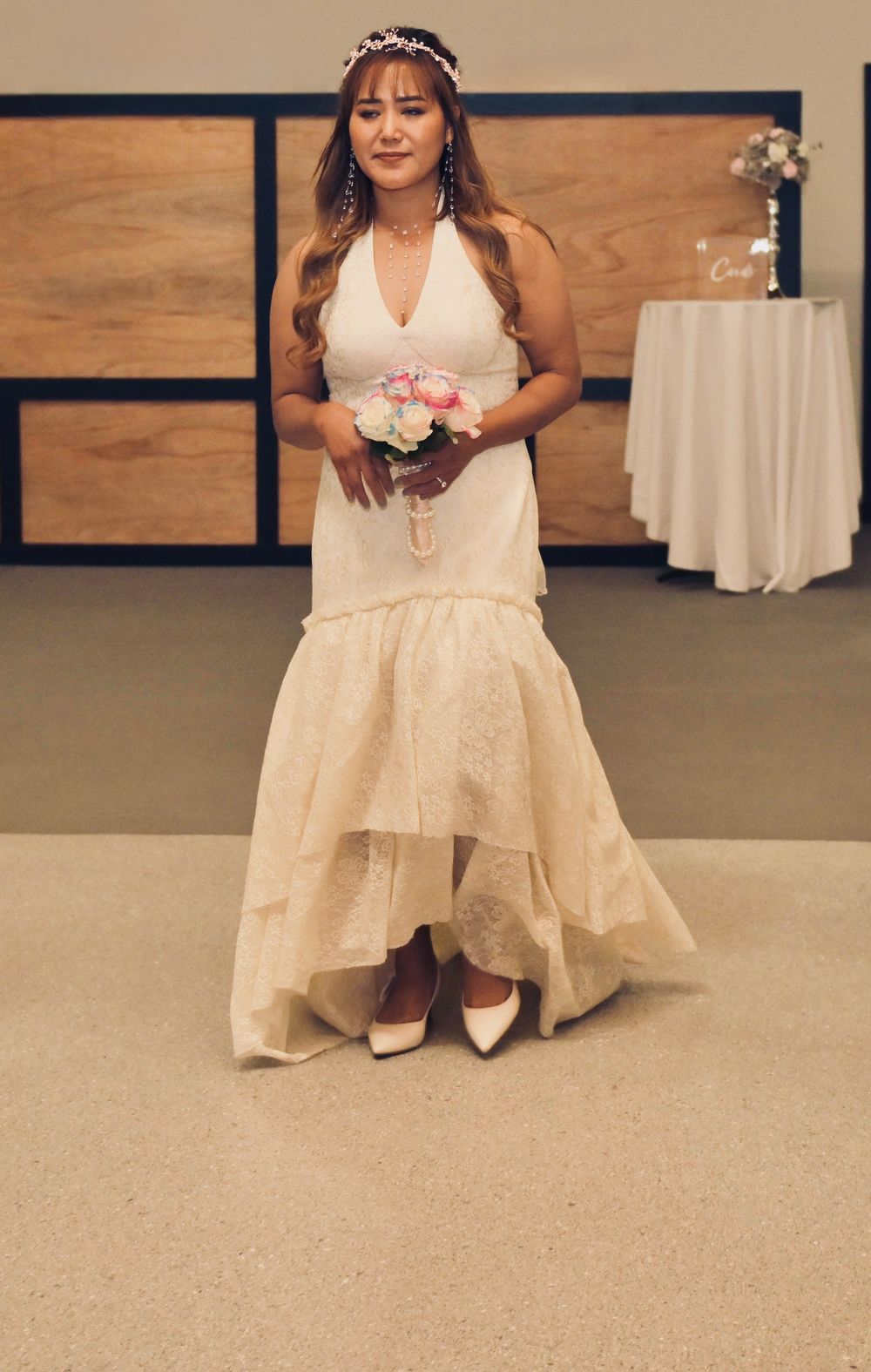 Bride in a halter mermaid wedding gown with tiered skirt holds a pink bouquet wearing a floral hair crown.