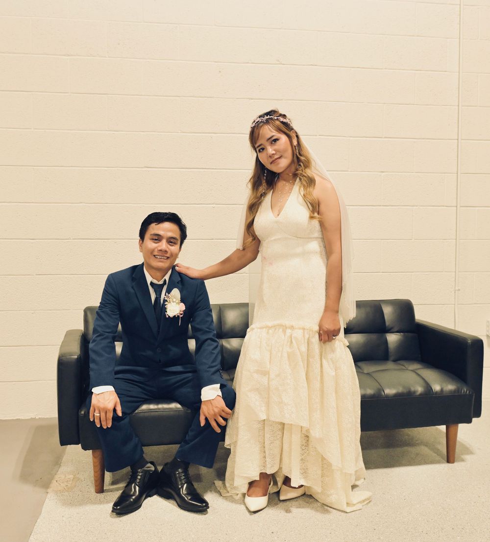 Bride in white halter dress and groom in navy suit posing together at wedding reception venue.