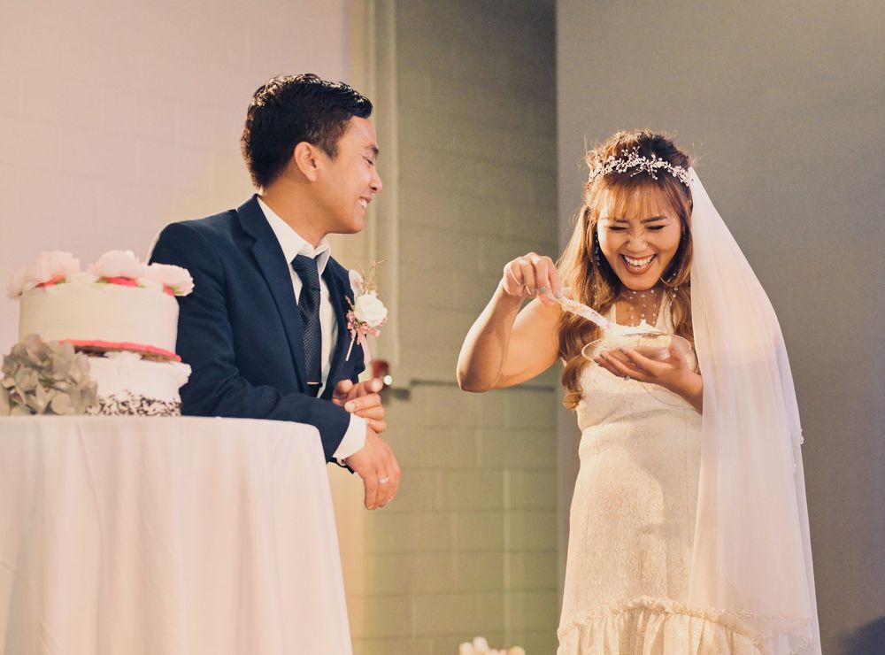 Happy couple cutting their wedding cake together, bride laughing in a white gown and veil.