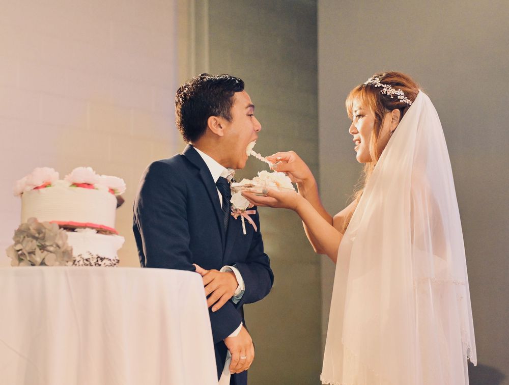 Bride feeding groom a piece of wedding cake during their reception celebration.
