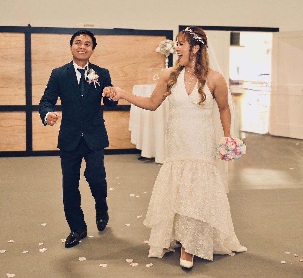 Smiling newlyweds walk together holding hands at wedding reception with rose petals on the floor.