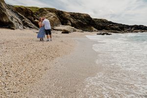 Couple walking hand in hand along a rocky secluded beach with gentle waves washing ashore.