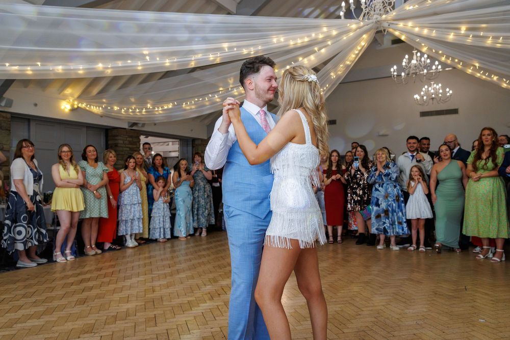 Bride and groom share their first dance at a wedding reception with guests watching in a decorated venue.