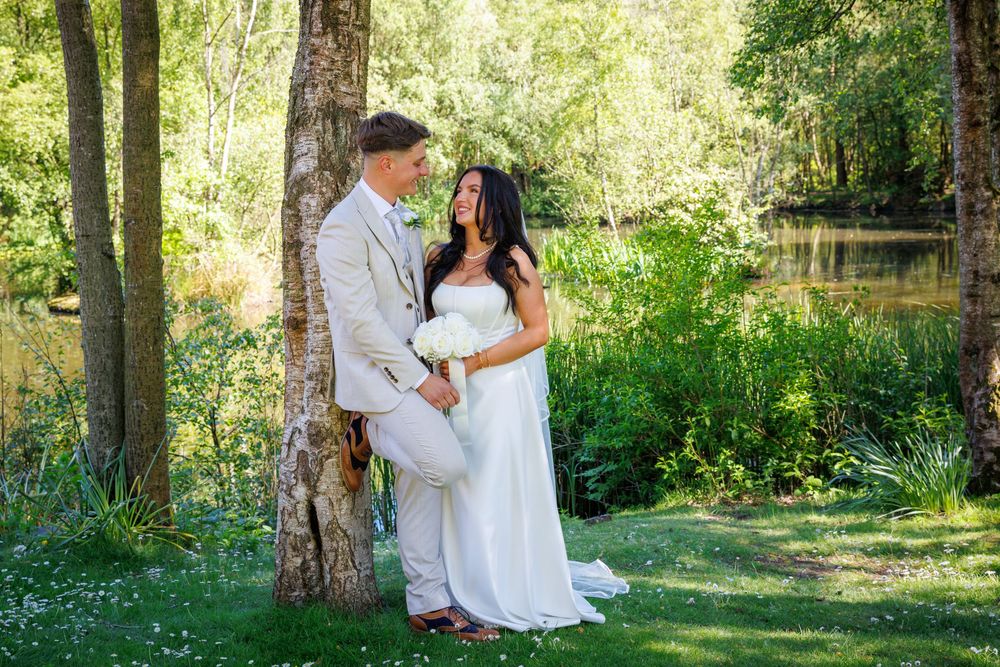 Bride and groom share romantic moment by tree in lush green garden setting on their wedding day.
