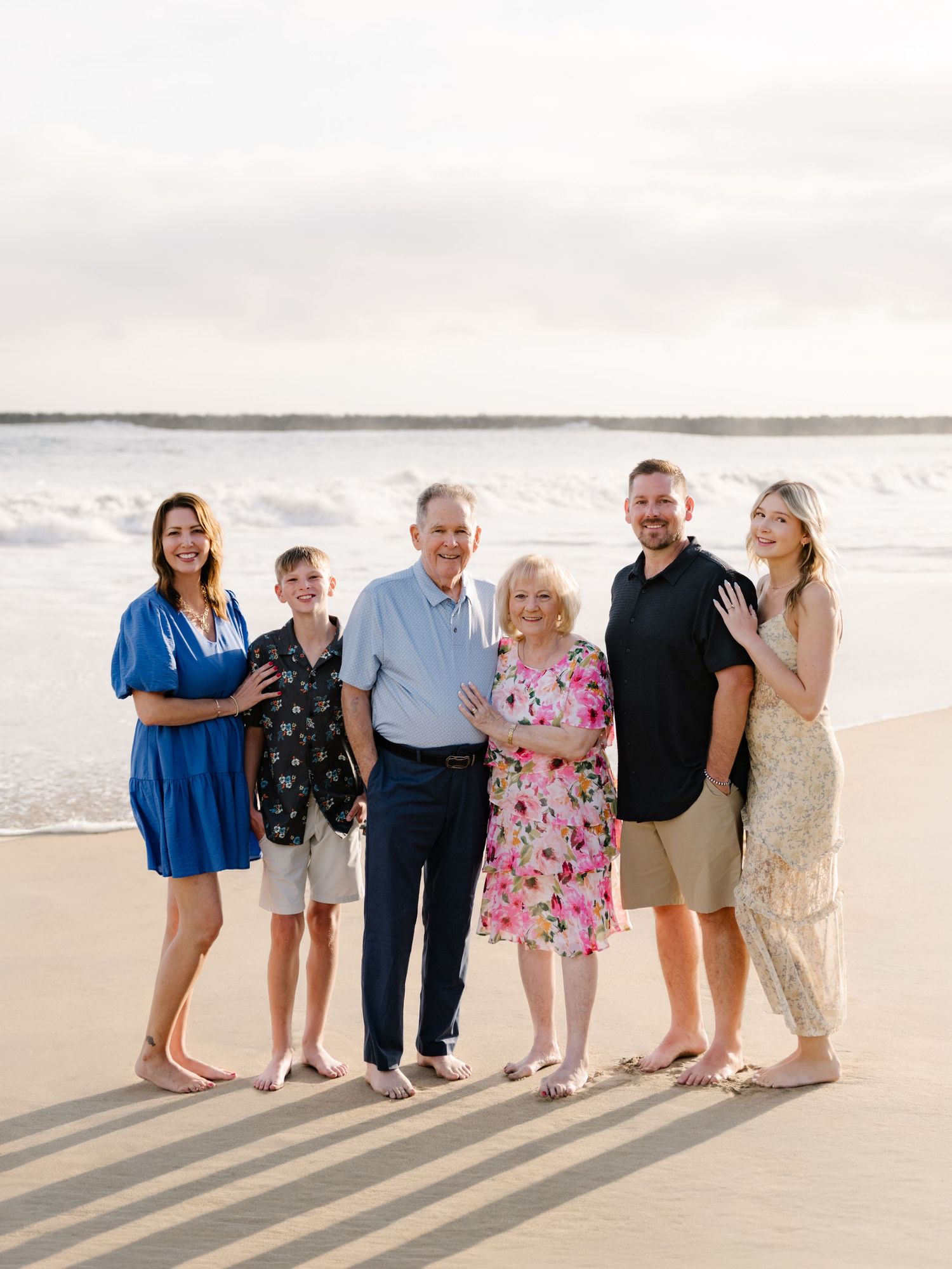 Three generations of family members smiling together on the beach during an Orange County extended family photography session.
