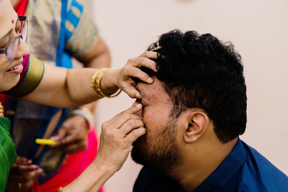 Woman applying kajal eyeliner to a man during an Indian wedding ceremony preparation.