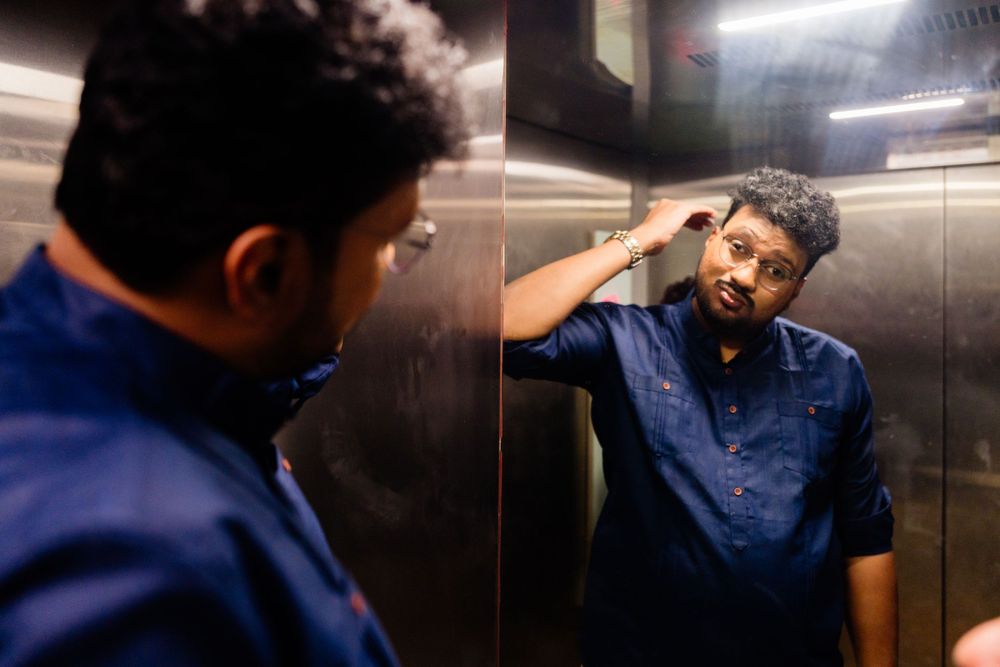 Indian man fixing his hair while looking at his reflection in an elevator mirror at a wedding event.