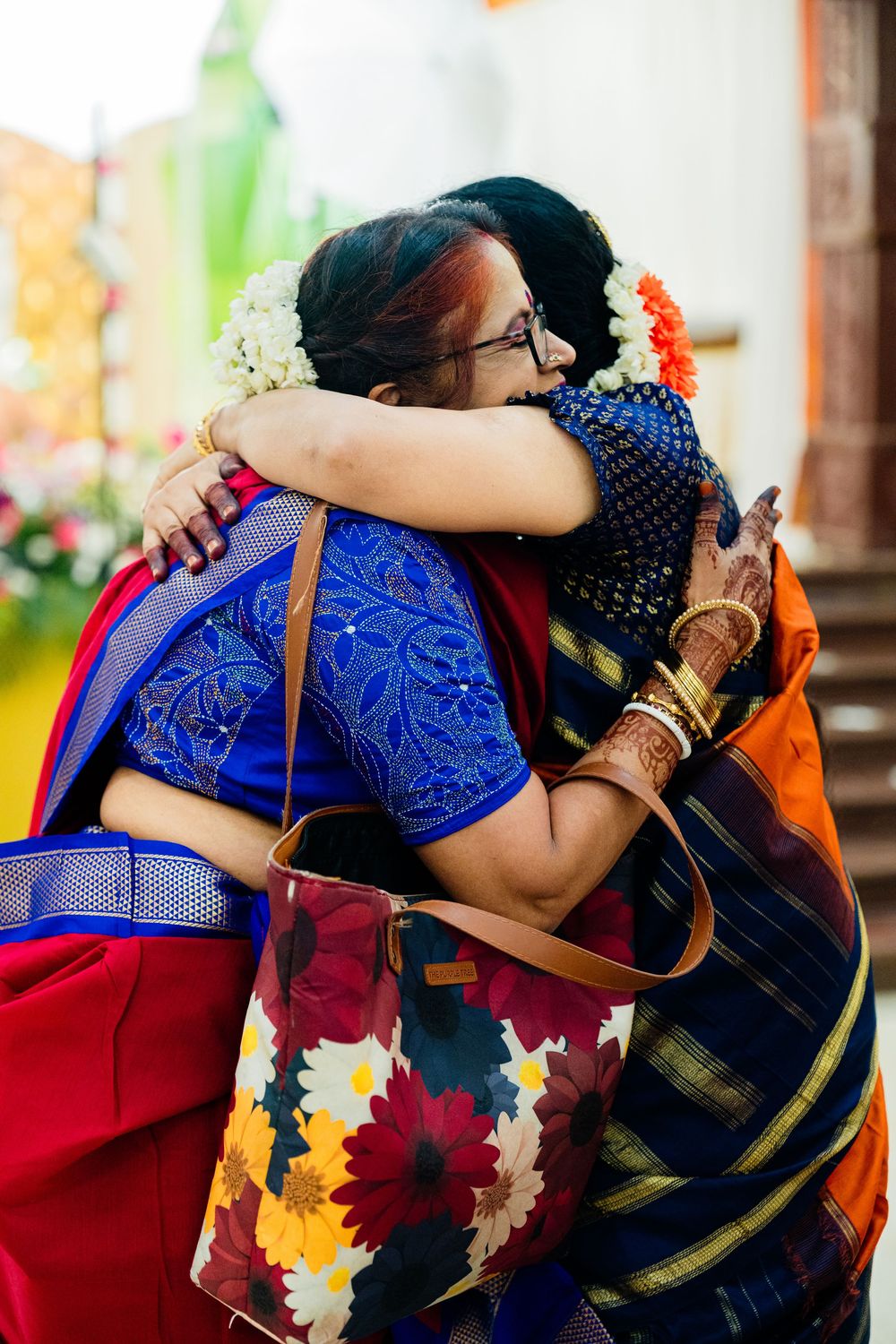 Two women in colorful silk sarees sharing a warm emotional hug at an Indian wedding celebration.