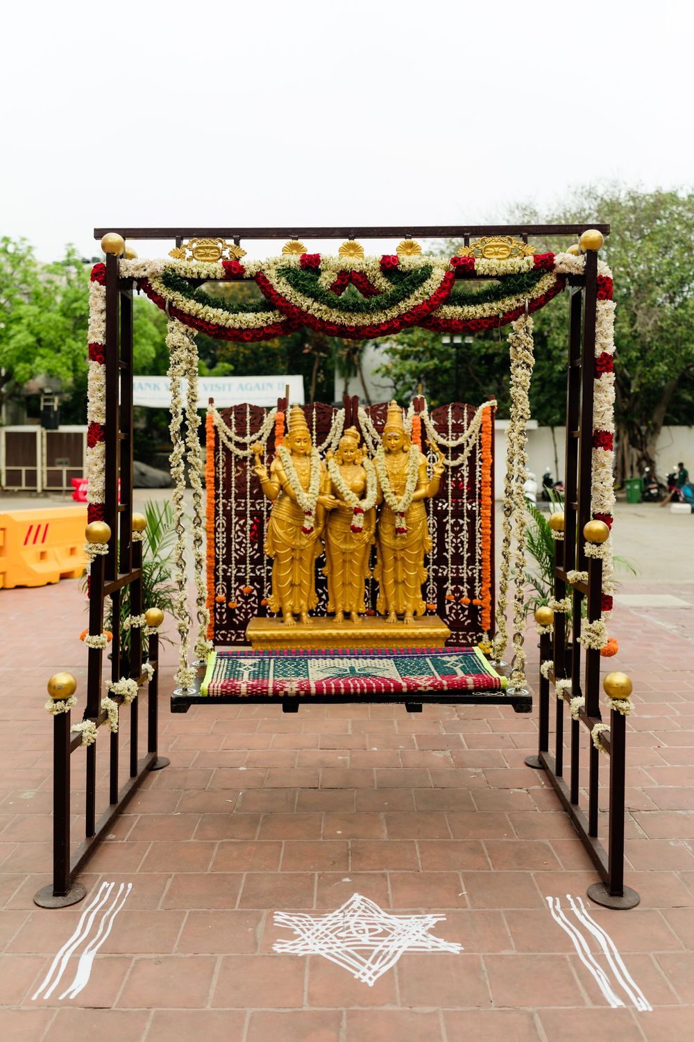 Golden Hindu deity statues on decorated swing mandap with floral garlands and rangoli at South Indian temple ceremony.