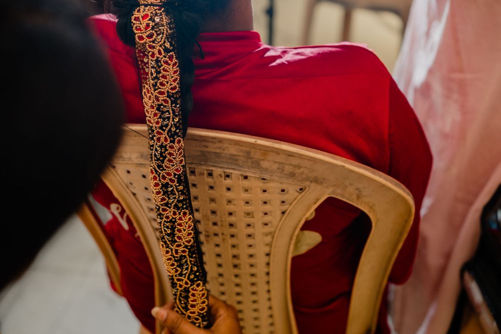 Close-up of a red silk garment with gold embroidered border draped over a woven wooden chair.