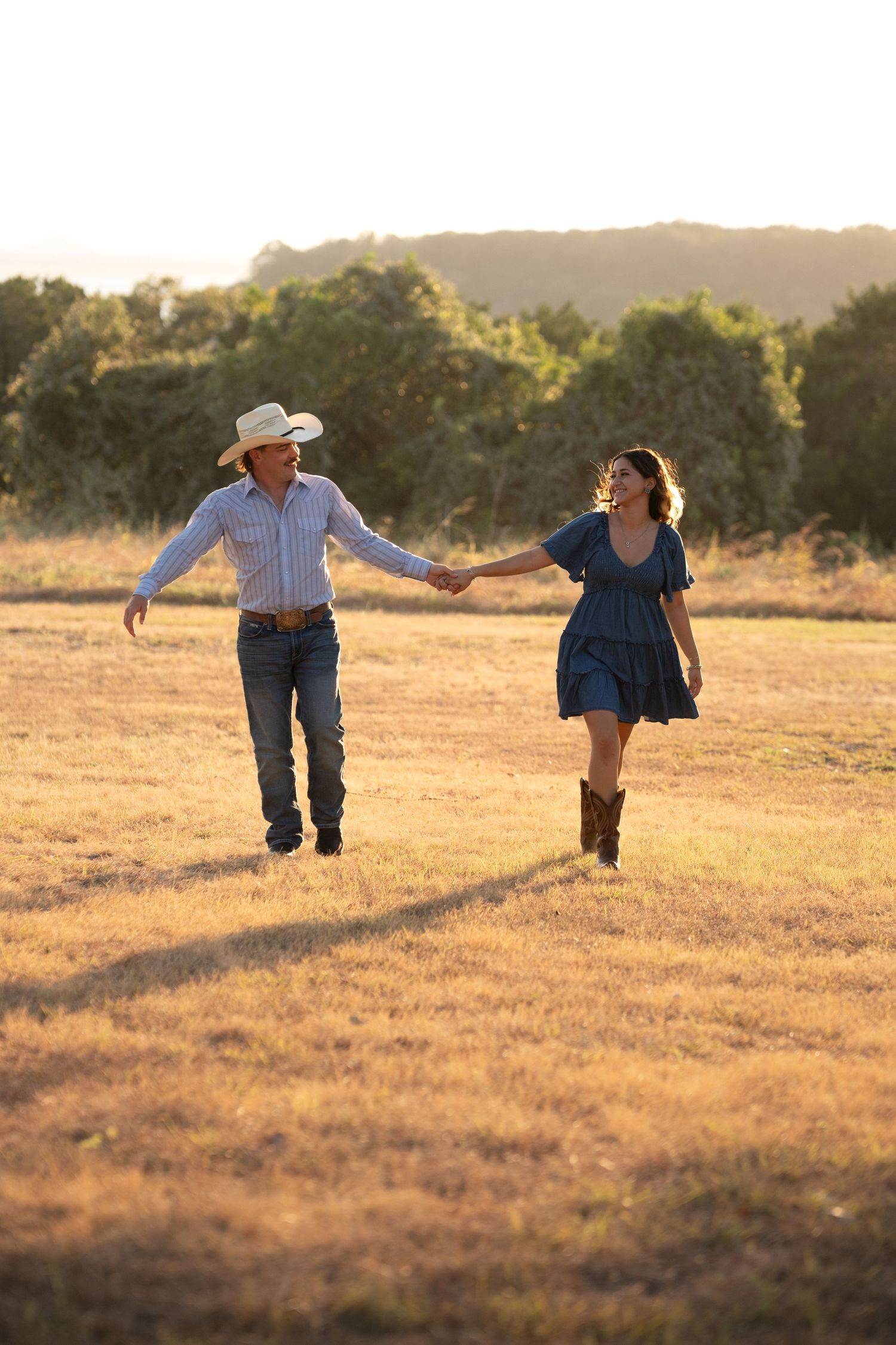 Couple holding hands and walking through a golden field at sunset in Belton Texas