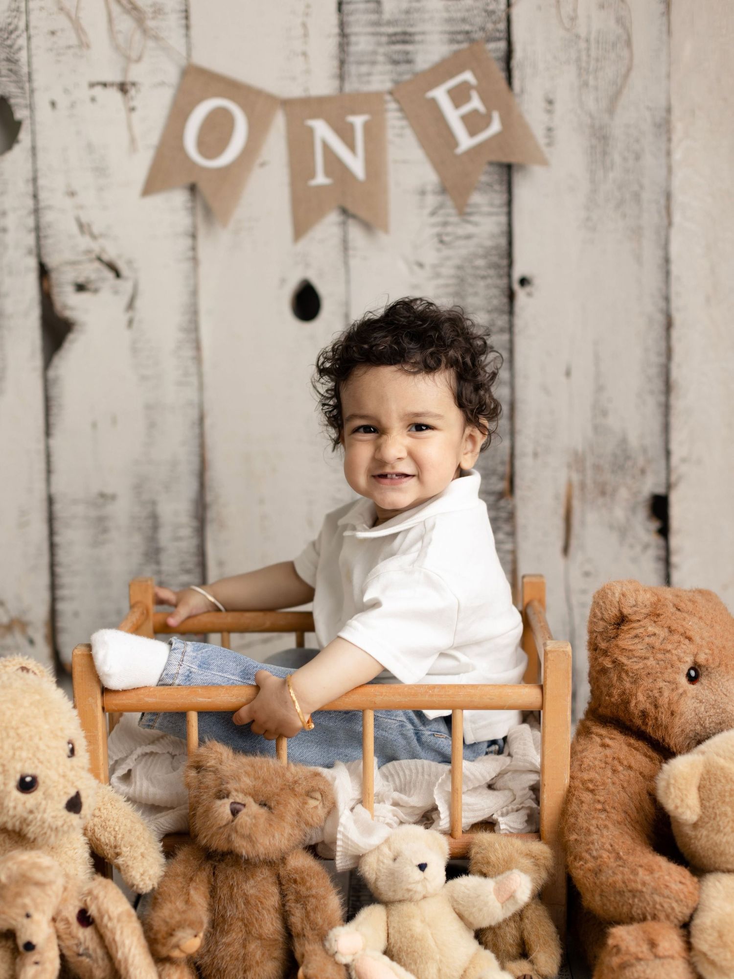 A young boy gently kisses a baby girl in a floral dress, sitting together in a charming rustic photo session.