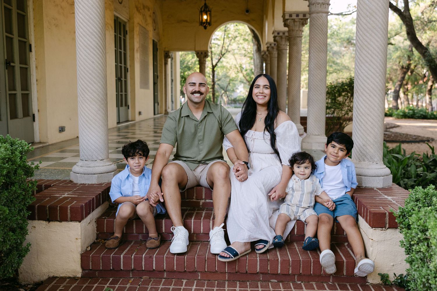 Happy family of five poses together on brick steps of an elegant home with columns in a portrait photo.