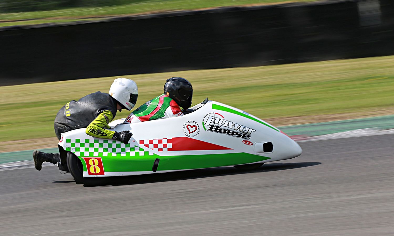 Racing sidecar number 8 with green and white checkered livery speeding on a circuit.