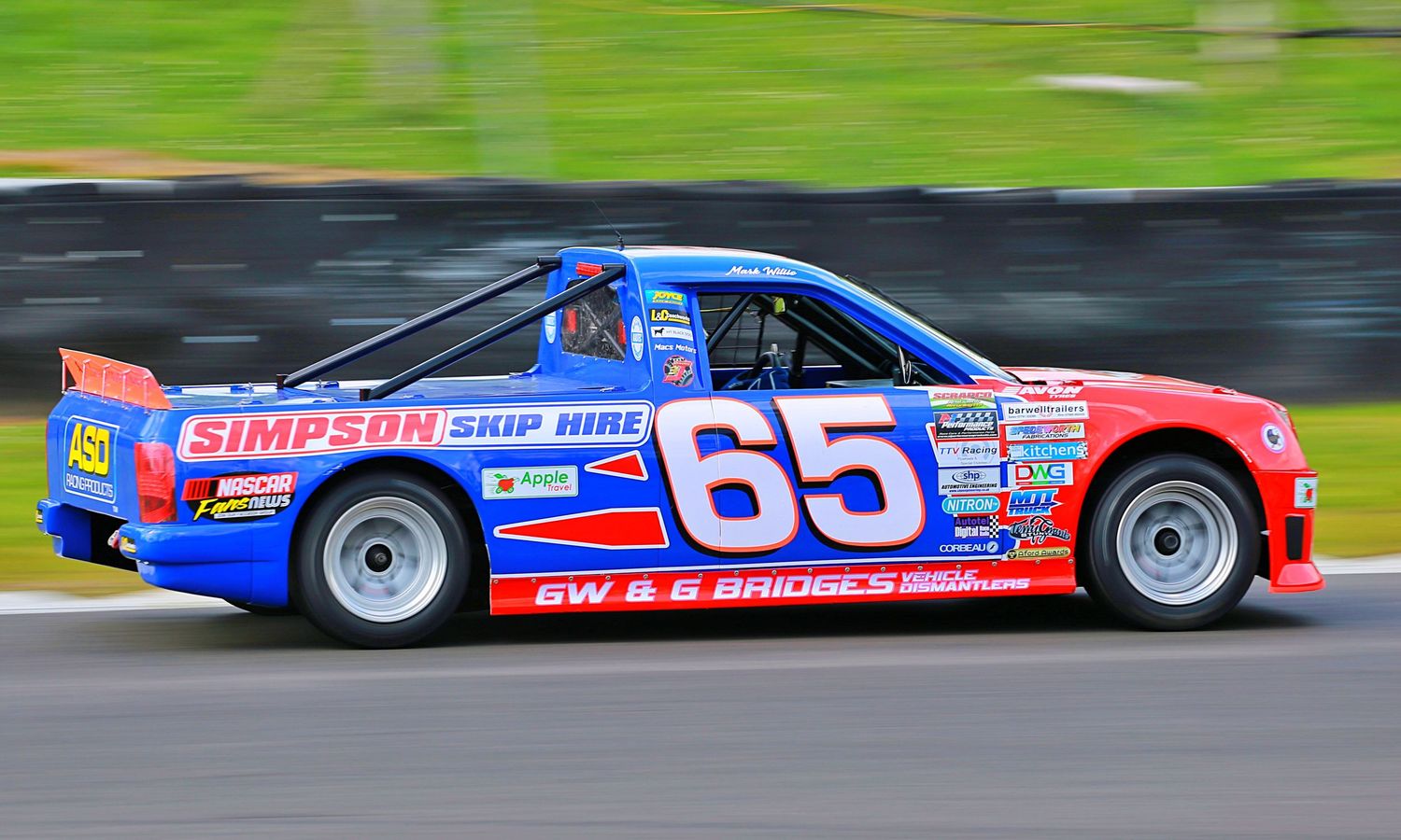 Blue and red number 65 Simpson Skip Hire stock car racing at high speed on a motorsport circuit.