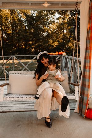 A mother and toddler laughing together on a white porch at The Holmstead Studio in Karns, TN with Nina Thomas Photography.