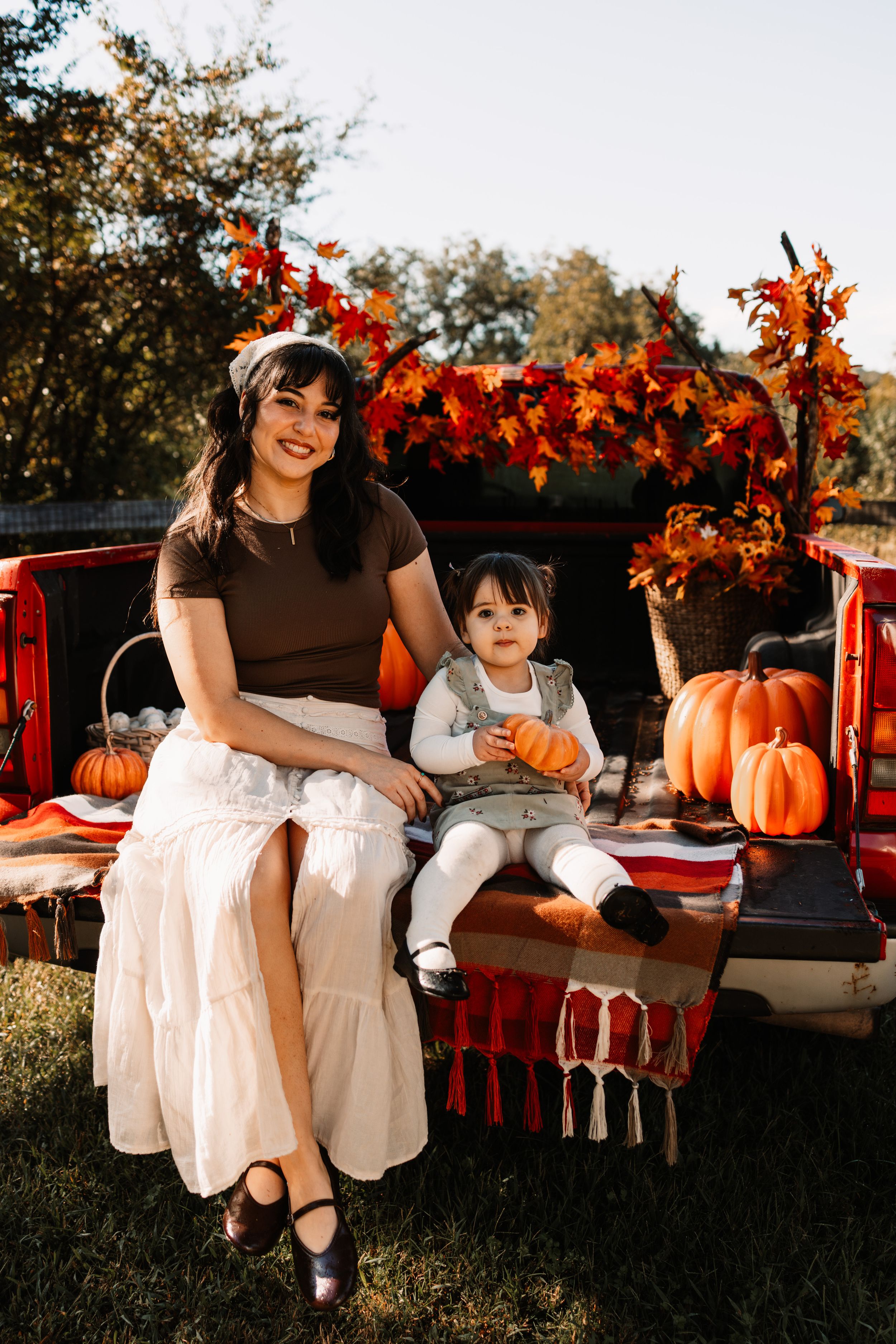 A mother and toddler sit on a decorated red truck tailgate at The Holmstead Studio in Karns, TN with Nina Thomas Photography.