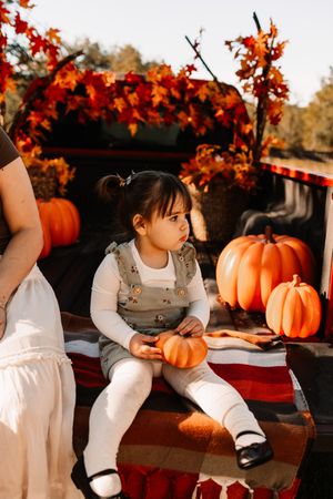 Toddler girl sitting in truck bed with pumpkins at The Holmstead Studio in Karns, TN with Nina Thomas Photography.