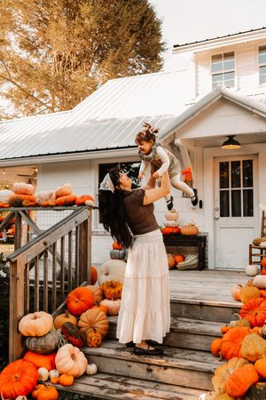 A mother lifts her child surrounded by colorful pumpkins on farmhouse at The Holmstead Studio in Karns, TN with Nina Thomas Photography.