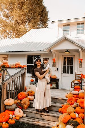Mother and daughter surrounded by colorful pumpkins at a white farmhouse decorated for fall at The Holmstead Studio in Karns, TN.