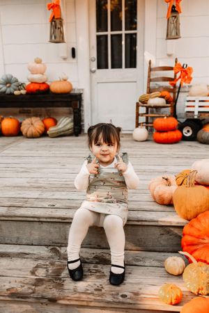 A cheerful toddler girl sits on a rustic wooden porch at The Holmstead Studio in Karns, TN with Nina Thomas Photography.