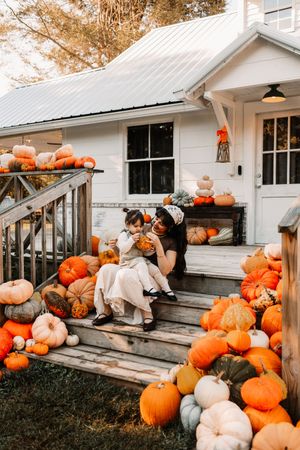 A mother and child sit on porch steps surrounded by pumpkins at The Holmstead Studio in Karns, TN with Nina Thomas Photography.