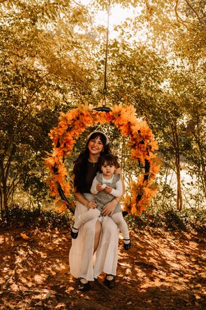 Woman and toddler sitting on a floral autumn wreath swing at The Holmstead Studio in Karns, TN with Nina Thomas Photography.