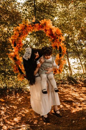 A mother holds her toddler on a fall leaf wreath swing outdoors at The Holmstead Studio in Karns, TN with Nina Thomas Photography.