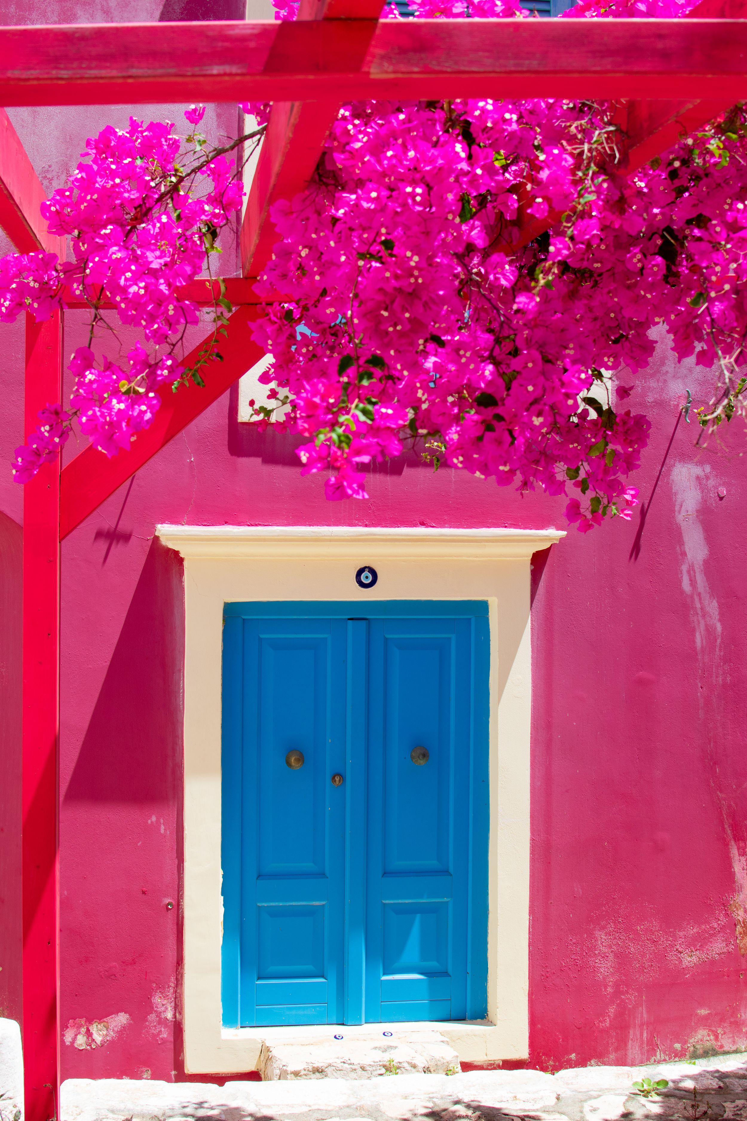 Vibrant pink bougainvillea cascading over a blue door on a hot pink wall in a Greek island setting.