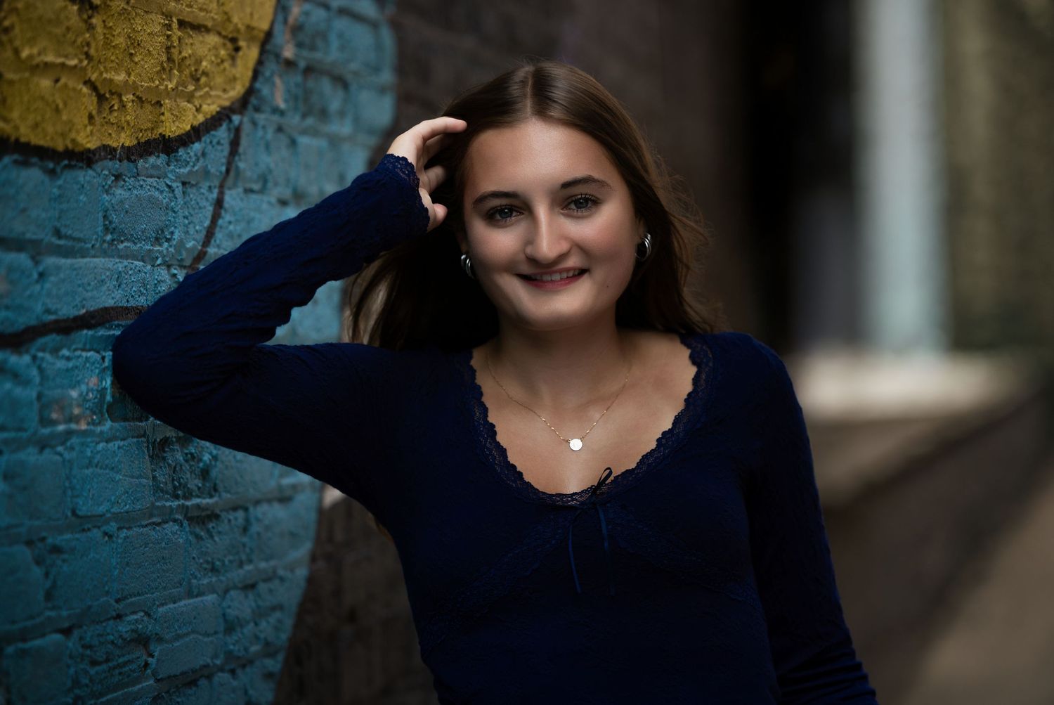 Senior portrait of a brunette girl beside a colorful brick wall