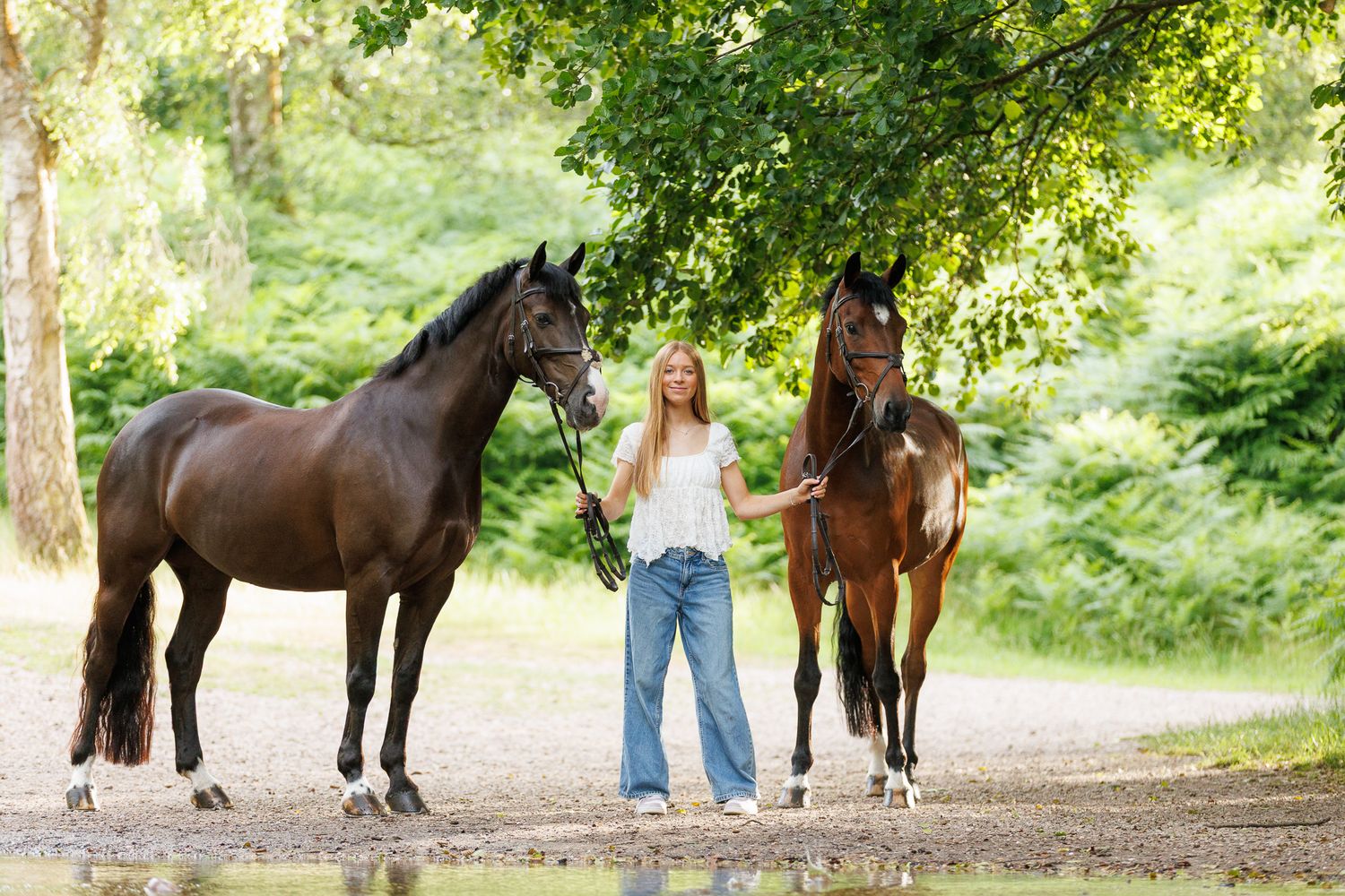 A woman sits on a log beside a brown horse in a field, holding its reins in a serene black and white photo.