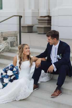 Bride and groom sitting on church steps, sharing a loving glance on their wedding day.