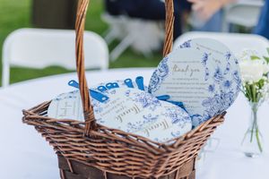 Wicker basket filled with blue and white floral paper fans and wedding programs at an outdoor ceremony.