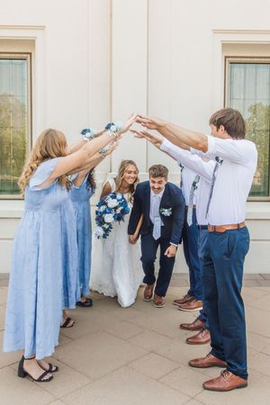 Wedding party celebrating bride and groom with raised hands arch outside venue.