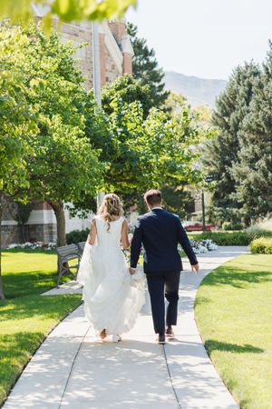 Bride and groom walking hand in hand down a sunny garden pathway on their wedding day.