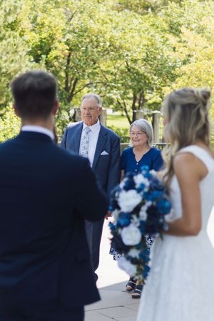 Elderly couple smiling warmly at bride and groom during outdoor wedding ceremony.