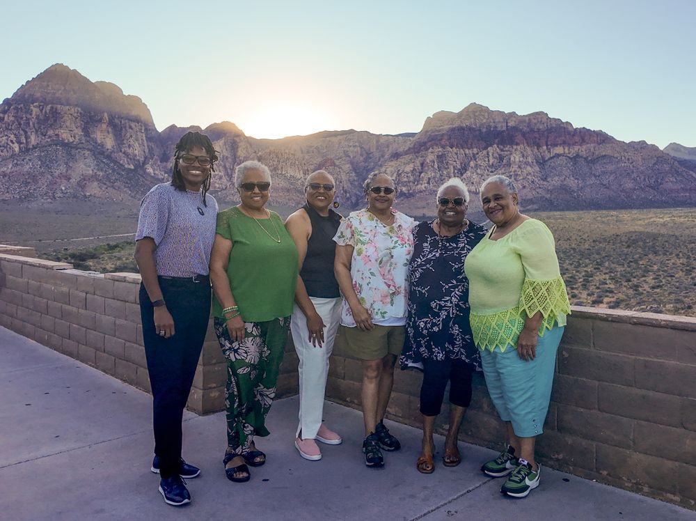 Six women pose together at Red Rock Canyon at sunset, with stunning desert mountains glowing in the background.