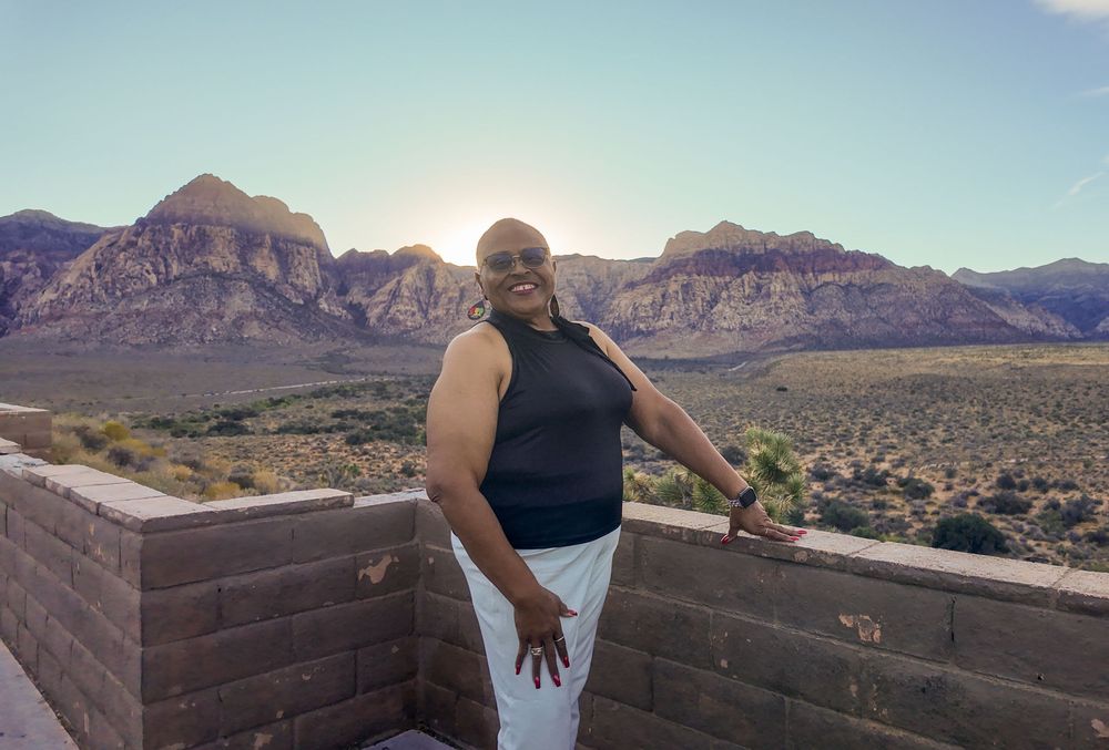 Woman smiling at Red Rock Canyon overlook, Nevada desert landscape and mountains in golden sunlight behind her.