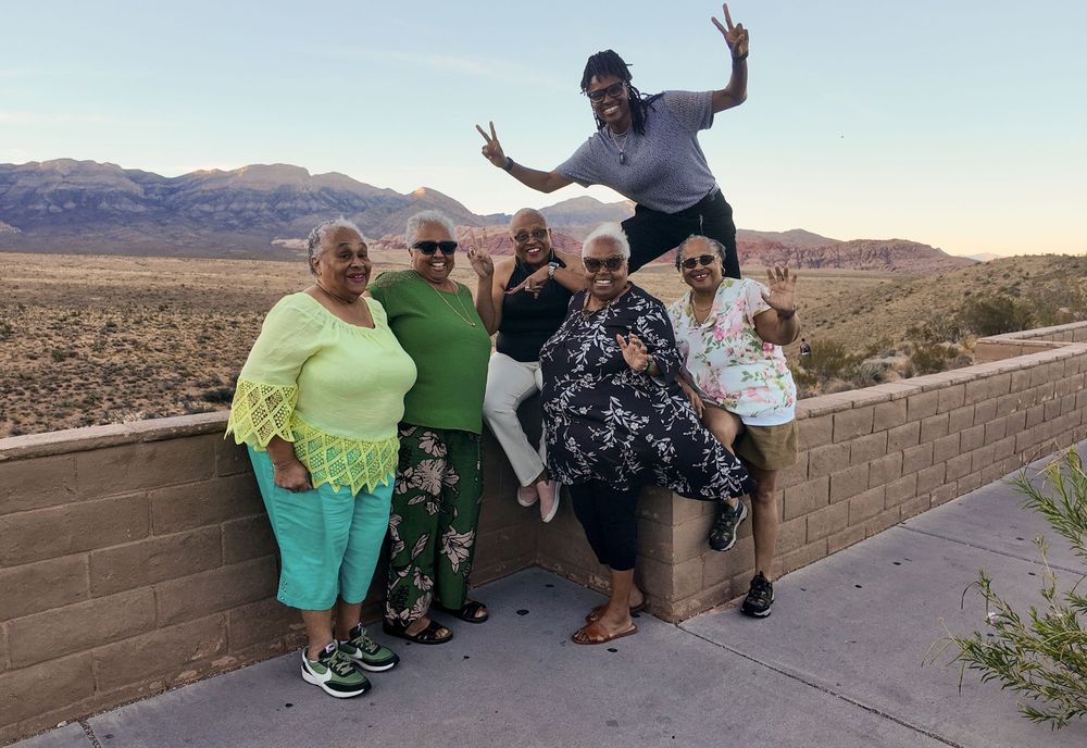 Group of friends posing and laughing at Red Rock Canyon overlook with desert mountains in background.