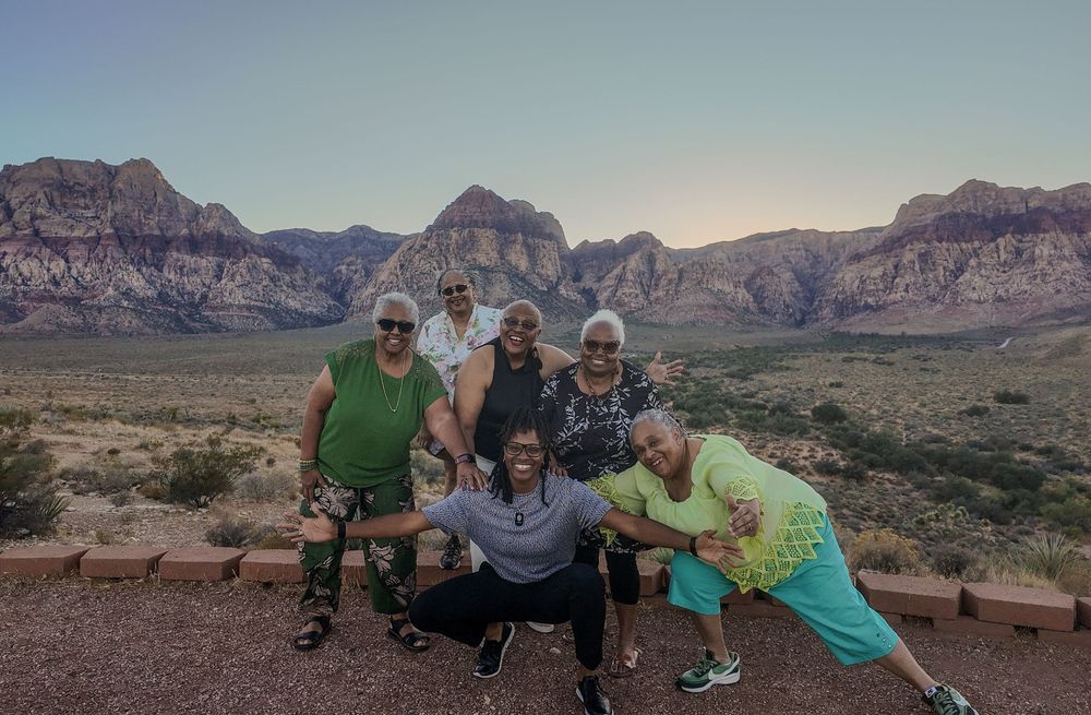 Group of six people posing at Red Rock Canyon scenic overlook with dramatic red rock formations at dusk.